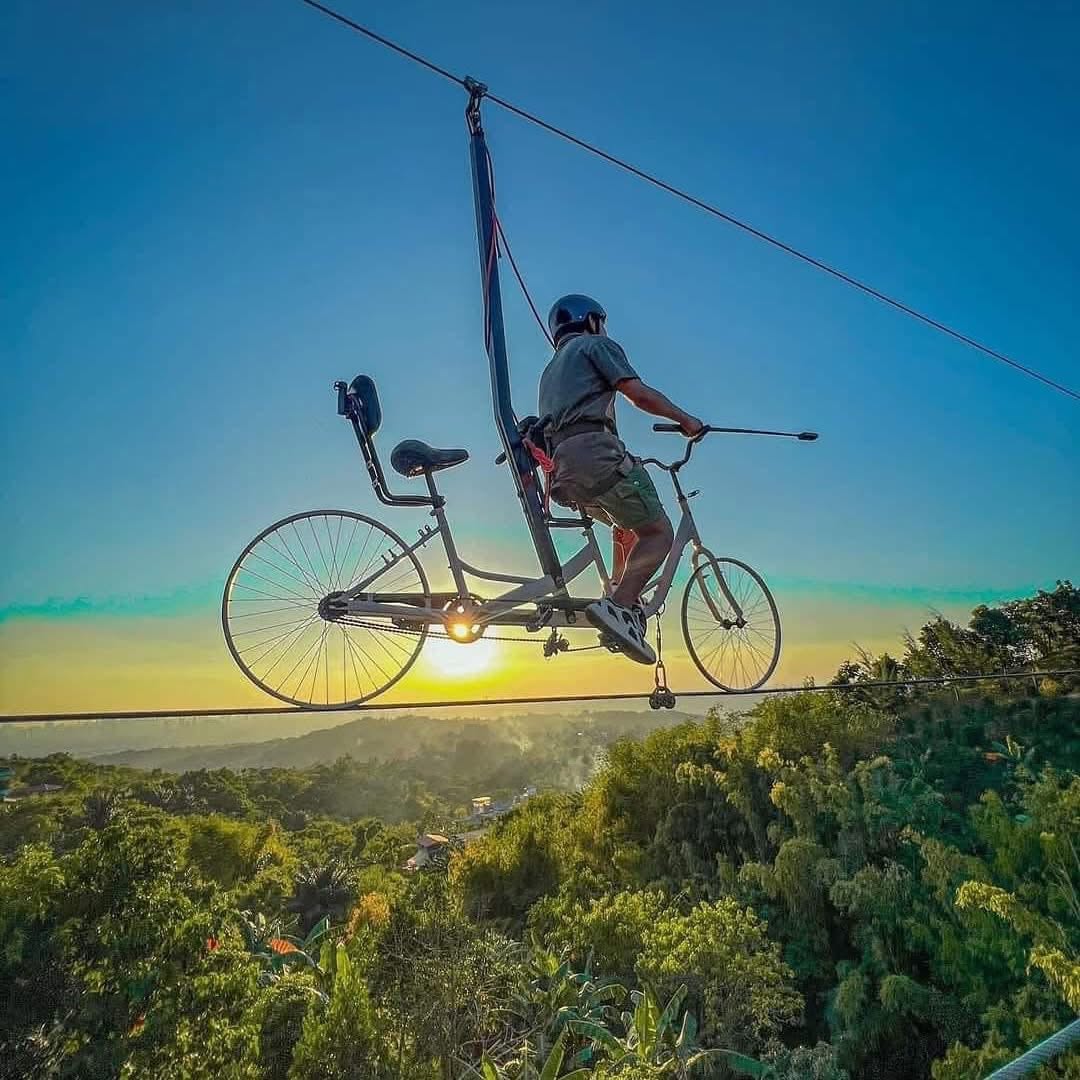 Rider pedaling a bicycle along an elevated cable above the landscape