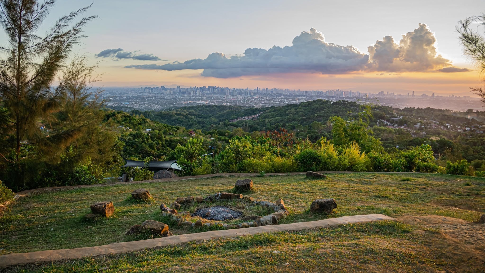 Open hillside viewpoint overlooking the city beneath a dramatic sunset sky